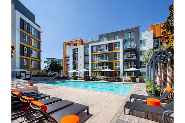 a pool with lounge chairs in front of an apartment building